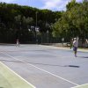 Campo da tennis con giocatori e alberi sullo sfondo.
