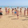 Bambini giocano sulla spiaggia, alzano le braccia verso il mare.