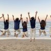 Gruppo di persone salta sulla spiaggia al tramonto.