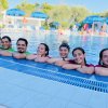 Otto persone sorridenti immerse nell'acqua di una piscina.