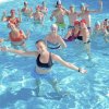 Persone in piscina con cuffie colorate, sorridono e salutano.