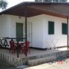 Bungalow bianco con tetto in legno, veranda con tavolo e sedie rosse.