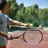 Un uomo pronto a servire una palla da tennis su un campo all'aperto.
