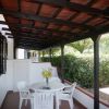 Terrazza coperta con tavolo rotondo e sedie bianche, circondata da siepi verdi.