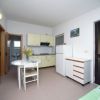 Cucina con tavolo rotondo, sedie, mobili chiari, frigorifero e bagno a vista.
