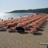 Una spiaggia con file di ombrelloni arancioni e gialli, bagnata dal mare.