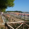 Spiaggia affollata con lettini e ombrelloni colorati, vista su torre in lontananza.