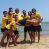 Gruppo di persone in maglia gialla che alzano un uomo in spiaggia.