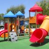 Parco giochi colorato con scivoli e torrette sotto alberi.