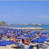 Spiaggia affollata con fila di ombrelloni blu sotto un cielo sereno.