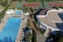 Vista dall'alto di una piscina e campi da tennis vicini a un edificio curvo.