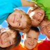 Gruppo di bambini sorridenti ripresi dal basso contro il cielo blu.