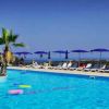 Piscina con palme al centro, sedie a sdraio e ombrelloni blu sullo sfondo.