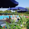 Piscina affollata con ombrelloni blu, sdraio e piante verdi intorno.
